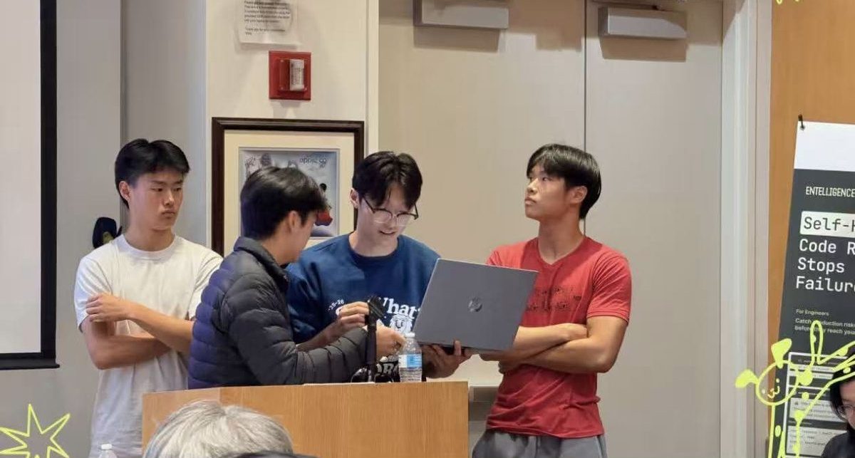 A team of four demos their project from a laptop at the podium